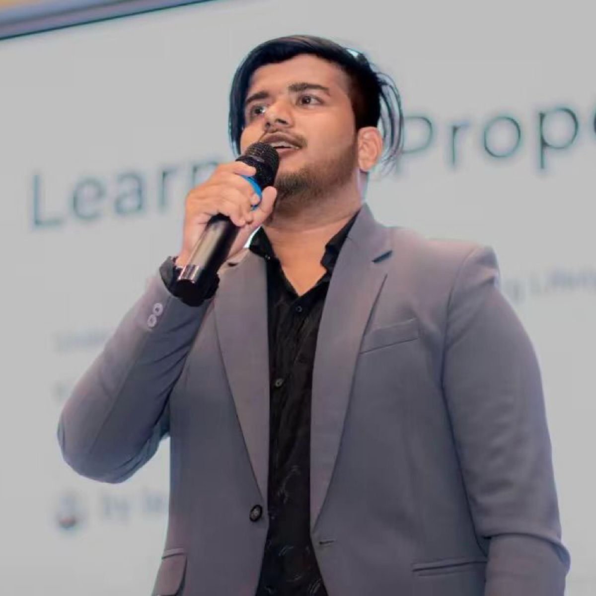 Isuru speaking into a microphone in a grey blazer